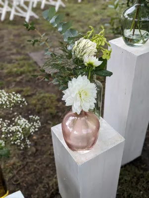 Composition décorative champêtre pour l'autel avec dahlia blanc, rose et eucalyptus sur des socles en bois.