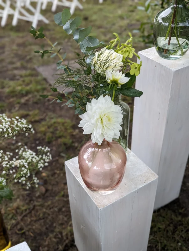 Composition décorative champêtre pour l'autel avec dahlia blanc, rose et eucalyptus sur des socles en bois.