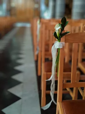 Détail de la décoration d'un banc d'église pour mariage, un petit bouquet d'arums blancs attaché avec un ruban délicat.