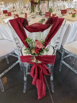 Chaise de table d'honneur de mariage décorée de draperies bordeaux, roses rouges et roses, et feuillage d'eucalyptus, style élégant.