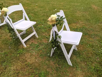 Décoration de chaises de cérémonie de mariage champêtre avec roses crème et feuillage.