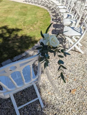 Décoration florale de chaise de cérémonie avec roses blanches et eucalyptus, pour un mariage élégant en extérieur.