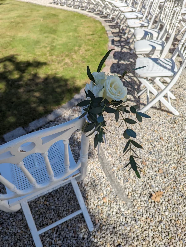 Ceremony chair floral decoration with white roses and eucalyptus, for an elegant outdoor wedding.