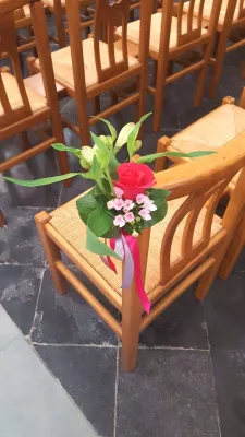 Décoration de chaise de cérémonie de mariage classique, avec une rose rouge, des petites fleurs roses et du feuillage vert.