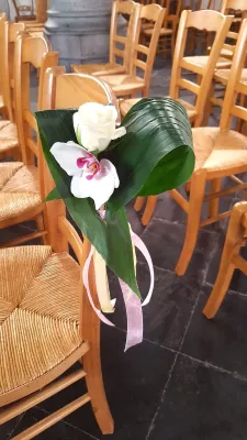 Décoration de chaise de cérémonie style classique avec une rose crème, une orchidée blanche et du feuillage vert plié.