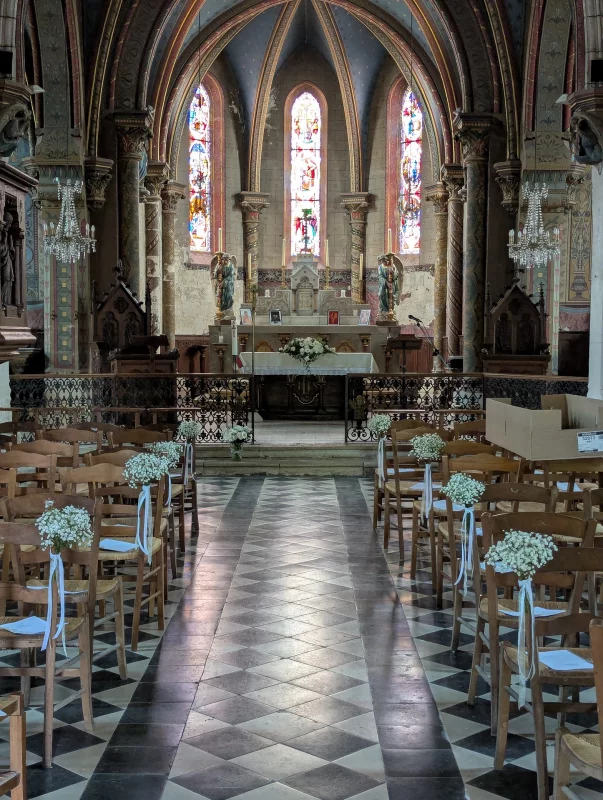 Décoration d'allée de cérémonie de mariage dans une église, avec des bouquets de gypsophile et rubans blancs sur les chaises.