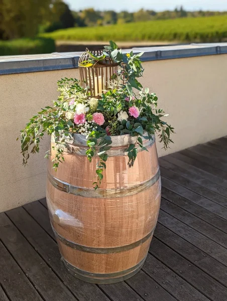 Décoration de fût en bois avec des roses crème, oeillets roses et feuillage tombant pour un mariage champêtre d'automne.