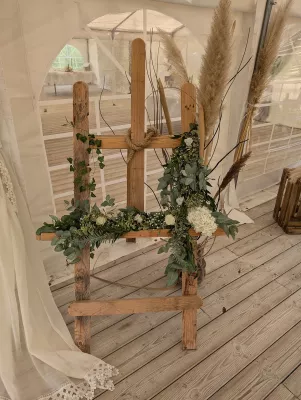 Décoration de panneau de bienvenue bohème avec eucalyptus, lierre, roses blanches, hortensias et herbe de pampas sur une structure en bois pour un mariage à Lanton.