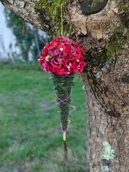 Décoration florale suspendue pour mariage, hortensias rouges, petites roses magenta, feuillage vert foncé, style bohème.
