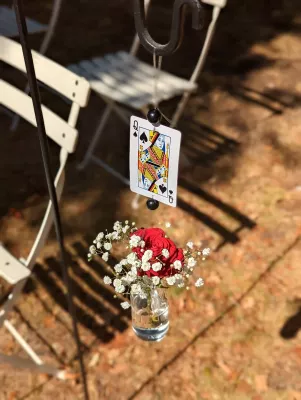 Petite décoration florale suspendue avec rose rouge, gypsophile blanc et carte à jouer, élégance classique pour cérémonie de mariage.