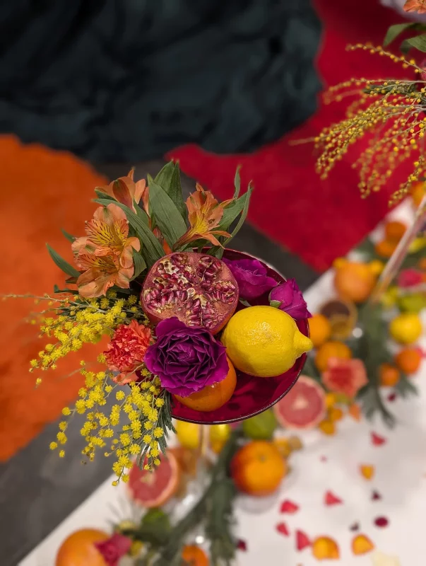 Decoration de table exotique avec grenade, citrons, oranges, roses pourpres et mimosa pour ceremonie.