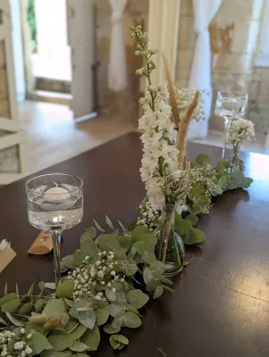 Décoration florale de table d'honneur bohème avec un chemin d'eucalyptus, delphinium et gypsophile.