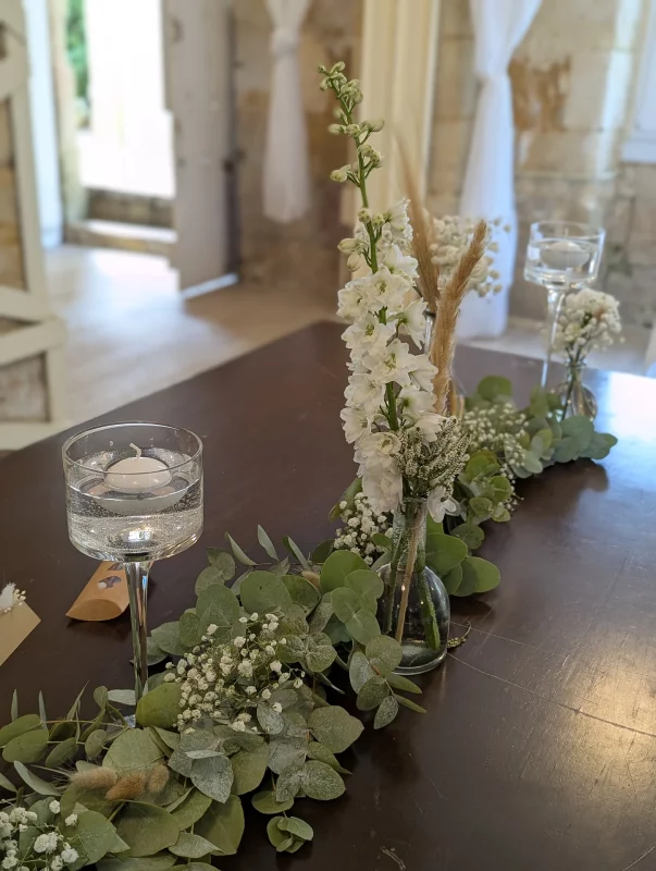 Décoration florale de table d'honneur bohème avec un chemin d'eucalyptus, delphinium et gypsophile.