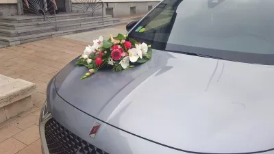 Composition florale pour capot de voiture de mariage, avec des orchidées blanches, des roses fuchsia et du feuillage.