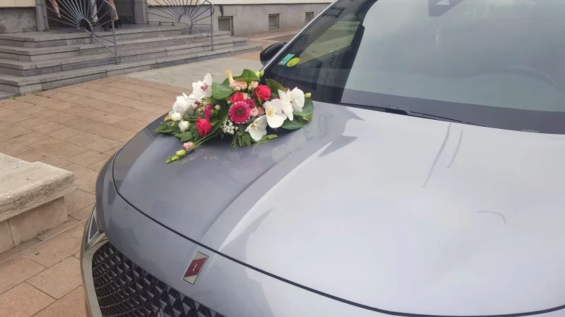 Composition florale pour capot de voiture de mariage, avec des orchidées blanches, des roses fuchsia et du feuillage.