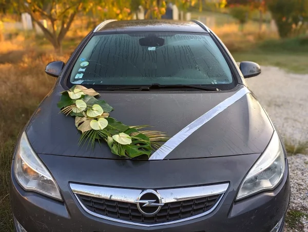 Décoration de voiture style exotique avec anthuriums blancs, feuilles de monstera et palmiers dorés pour un mariage.