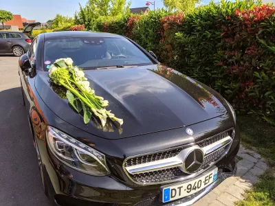 Décoration florale de voiture de mariage classique, avec un élégant arrangement d'arums et roses blanches sur le capot.