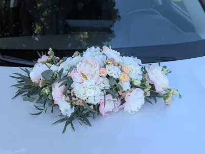 Décoration florale de voiture de mariage classique, avec des pivoines, des roses pêche et de l'eucalyptus frais.