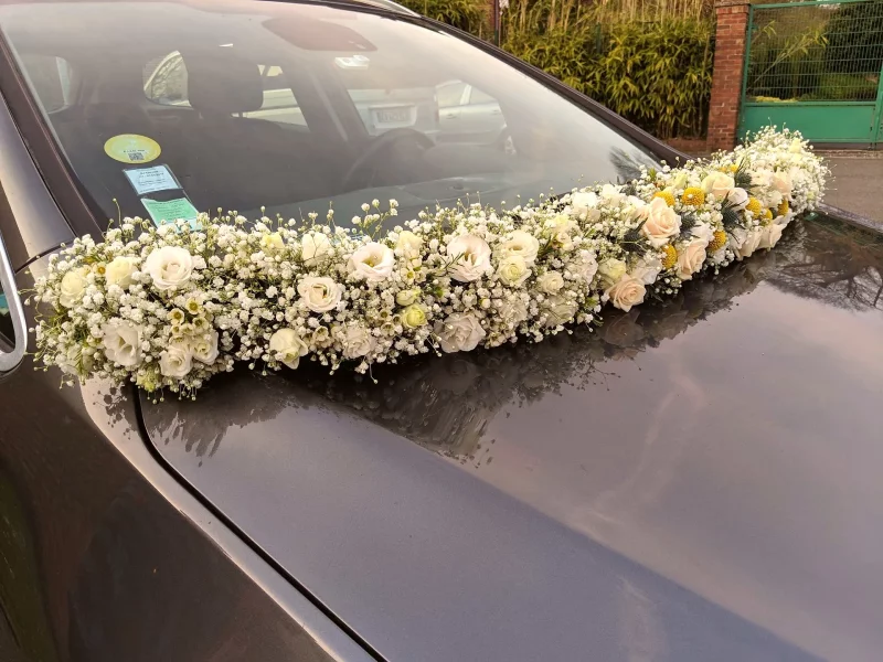 Décoration de voiture de mariage classique avec roses blanches, gypsophile et touches de jaune, ambiance printanière douce.