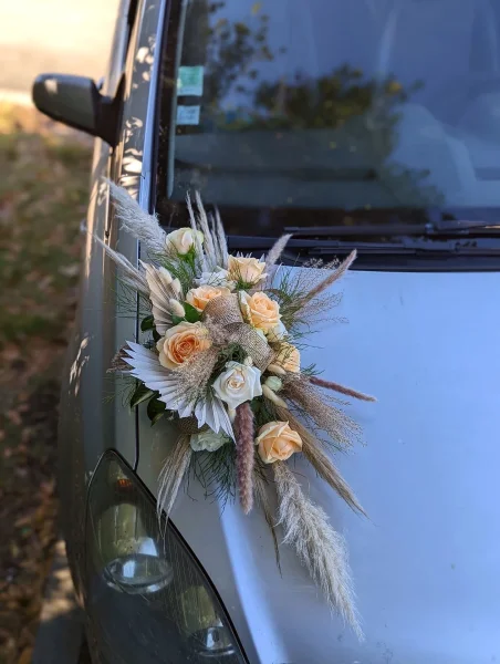 Décoration de voiture boheme avec roses pêche et pampas, feuilles de palmier pour un mariage en été.