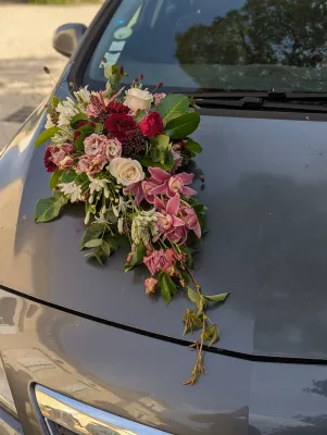 Décoration florale de voiture de mariage bohème avec roses crème, bordeaux, orchidées roses et eucalyptus pour une allure élégante.