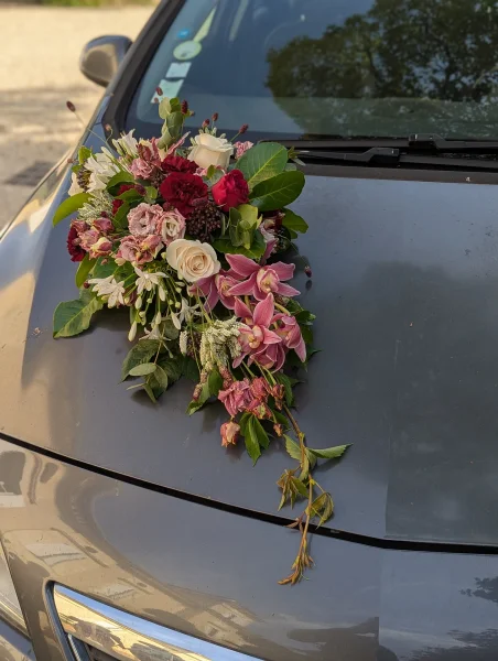 Décoration florale de voiture de mariage bohème avec roses crème, bordeaux, orchidées roses et eucalyptus pour une allure élégante.