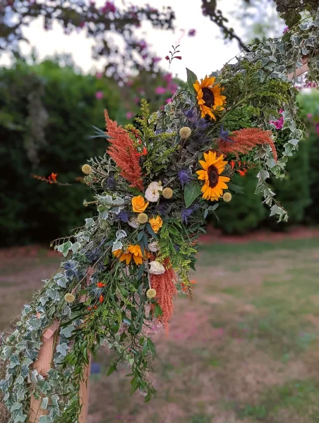 Gros plan sur la décoration de l'arche florale champêtre avec tournesols, chardons et lierre.