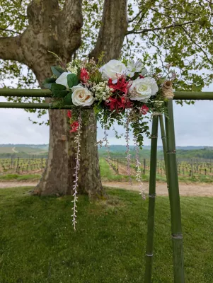 Détail d'arche florale exotique pour mariage, roses blanches et crèmes, fleurs rouges, feuillage retombant.