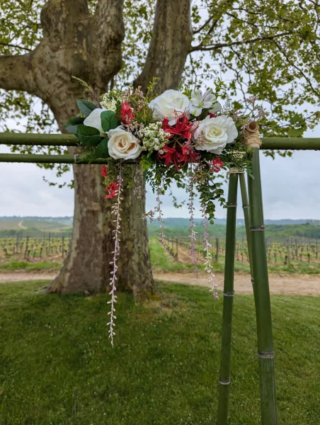 Détail d'arche florale exotique pour mariage, roses blanches et crèmes, fleurs rouges, feuillage retombant.