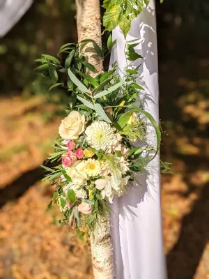 Gros plan sur la décoration florale d'une arche de mariage, avec des roses blanches, des dahlias et un feuillage verdoyant.