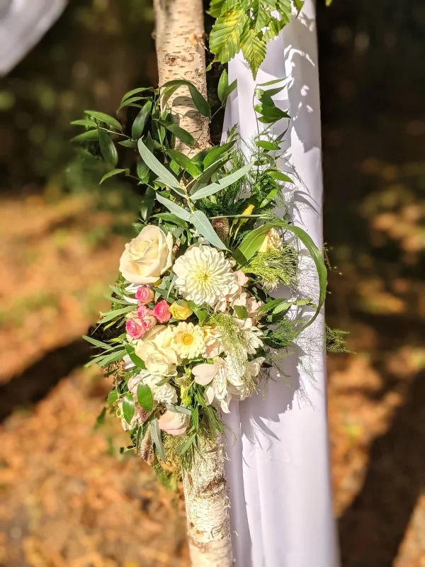 A close-up of the floral decoration on a floral arch, with white roses, dahlias and lush greenery.