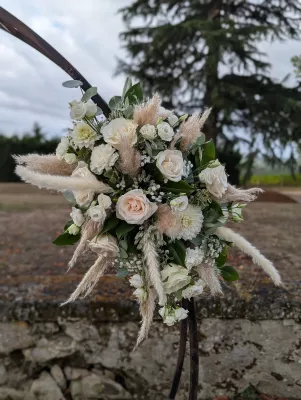Gros plan sur la décoration florale de l'arche de mariage bohème, avec roses, pampa et feuillage vert.