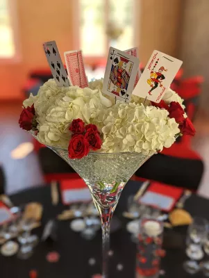 Gros plan d'un centre de table classique avec hortensias blancs, roses rouges et cartes à jouer, détail floral de mariage.