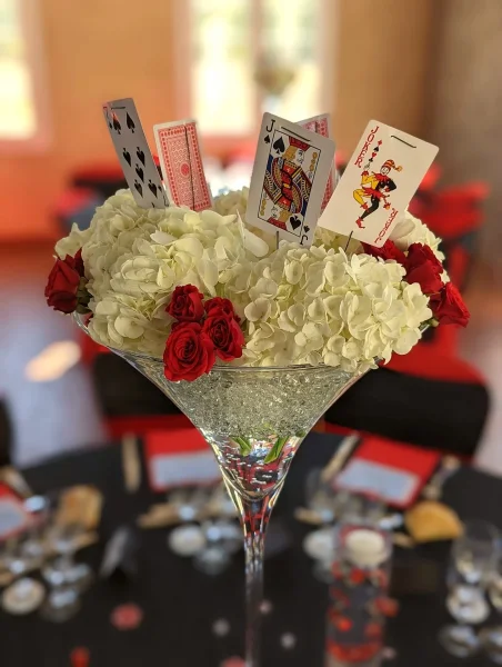 Gros plan d'un centre de table classique avec hortensias blancs, roses rouges et cartes à jouer, détail floral de mariage.