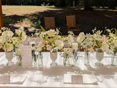 Gros plan sur un centre de table de mariage avec roses, dahlias, alstroemerias, bougies, vases en verre et marques-places.