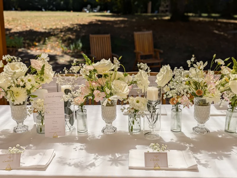Close-up on a wedding table centrepiece featuring roses, dahlias, alstroemerias, candles, glass vases, and place cards.