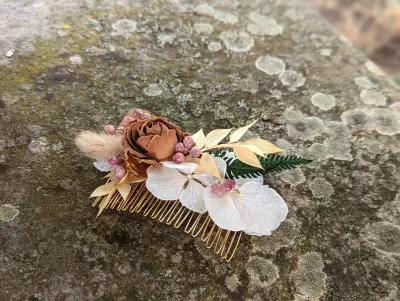 Peigne floral de coiffure bohème avec rose séchée, hortensia blanc cassé et feuillage doré, sur une base métallique.