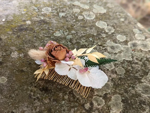 Peigne floral de coiffure bohème avec rose séchée, hortensia blanc cassé et feuillage doré, sur une base métallique.