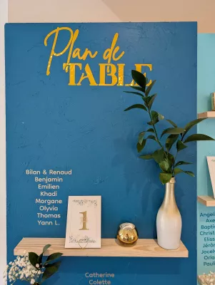 Bilane & Renaud wedding table plan, sophisticated country style, with green foliage and gold vase on a blue background.