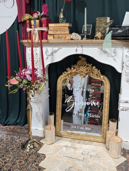 Décoration de cheminée vintage avec miroir doré orné, chandelier fleuri, livres et pages dispersées, ambiance romantique.