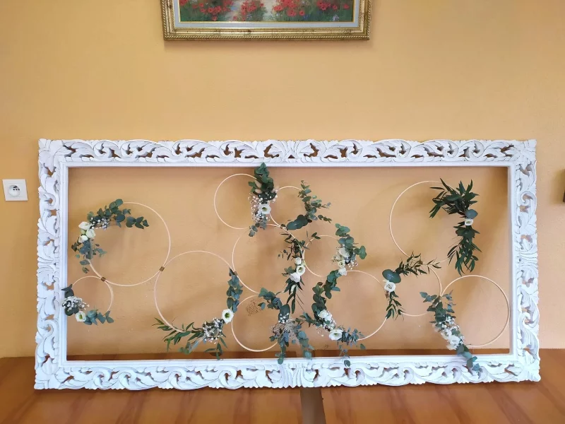 Scénographie florale murale champêtre avec cercles décorés d'eucalyptus, roses blanches et gypsophile, créant une ambiance naturelle.