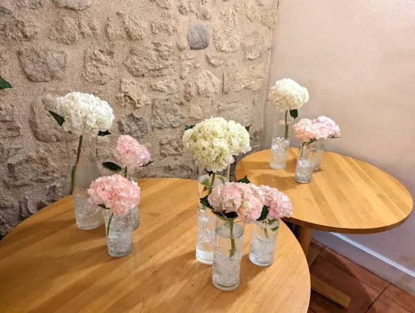 Scénographie champêtre pour mariage avec bouquets d'hortensias blancs et roses dans des vases en verre.