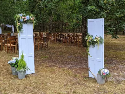 Scénographie d'entrée de mariage bohème avec portes anciennes fleuries d'hortensias bleus et roses, et un arrosoir vintage.