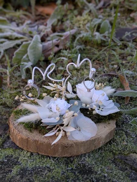Support d'alliances bohème chic pour un mariage, avec roses blanches, eucalyptus et fleurs séchées.