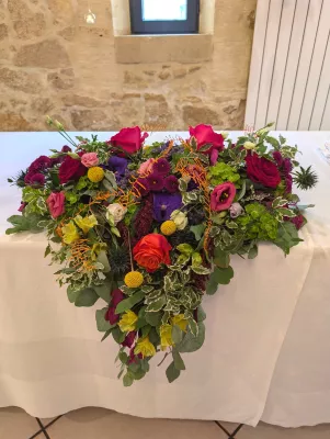 Composition florale en cascade pour table d'honneur, roses rouges, chardons bleus, feuillages panachés, mariage à Barsac.