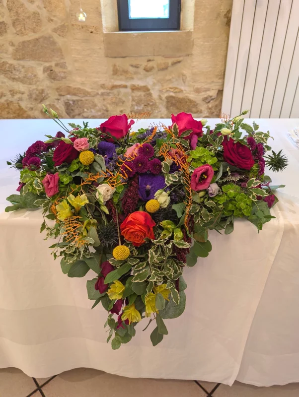 Composition florale en cascade pour table d'honneur, roses rouges, chardons bleus, feuillages panachés, mariage à Barsac.