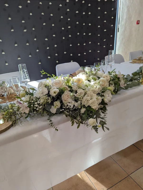 Sophisticated country-style head table floral decoration with roses and eucalyptus for a wedding.