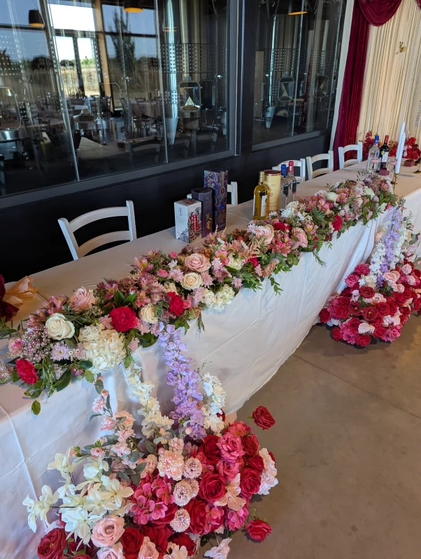 Sophisticated country-style head table with fuchsia roses, white lisianthus, and purple delphiniums for Marina & Frédéric's wedding.