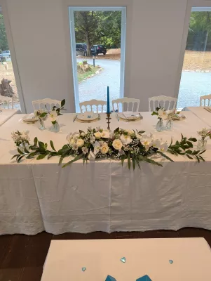 Head table floral decoration with roses, orchids, gypsophila, and green foliage.