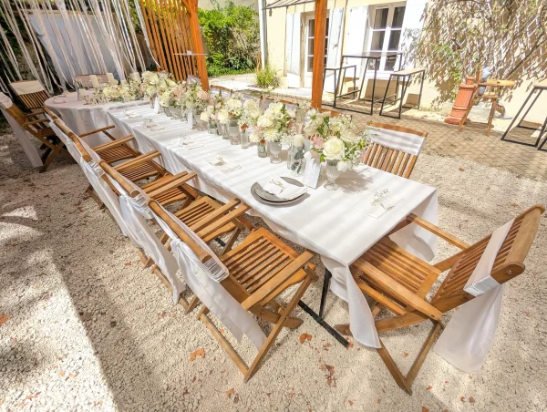 Vue d'ensemble d'une longue table de réception de mariage avec centres de table floraux blancs et roses, chaises en bois et nappes blanches.